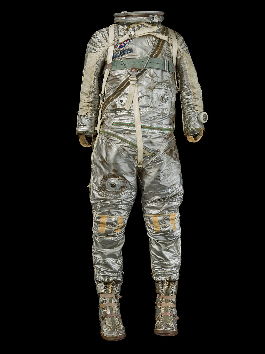 Reflective silver Mercury pressure suit displayed with white helmet, silver gloves and boots, straps, hoses, and valves.