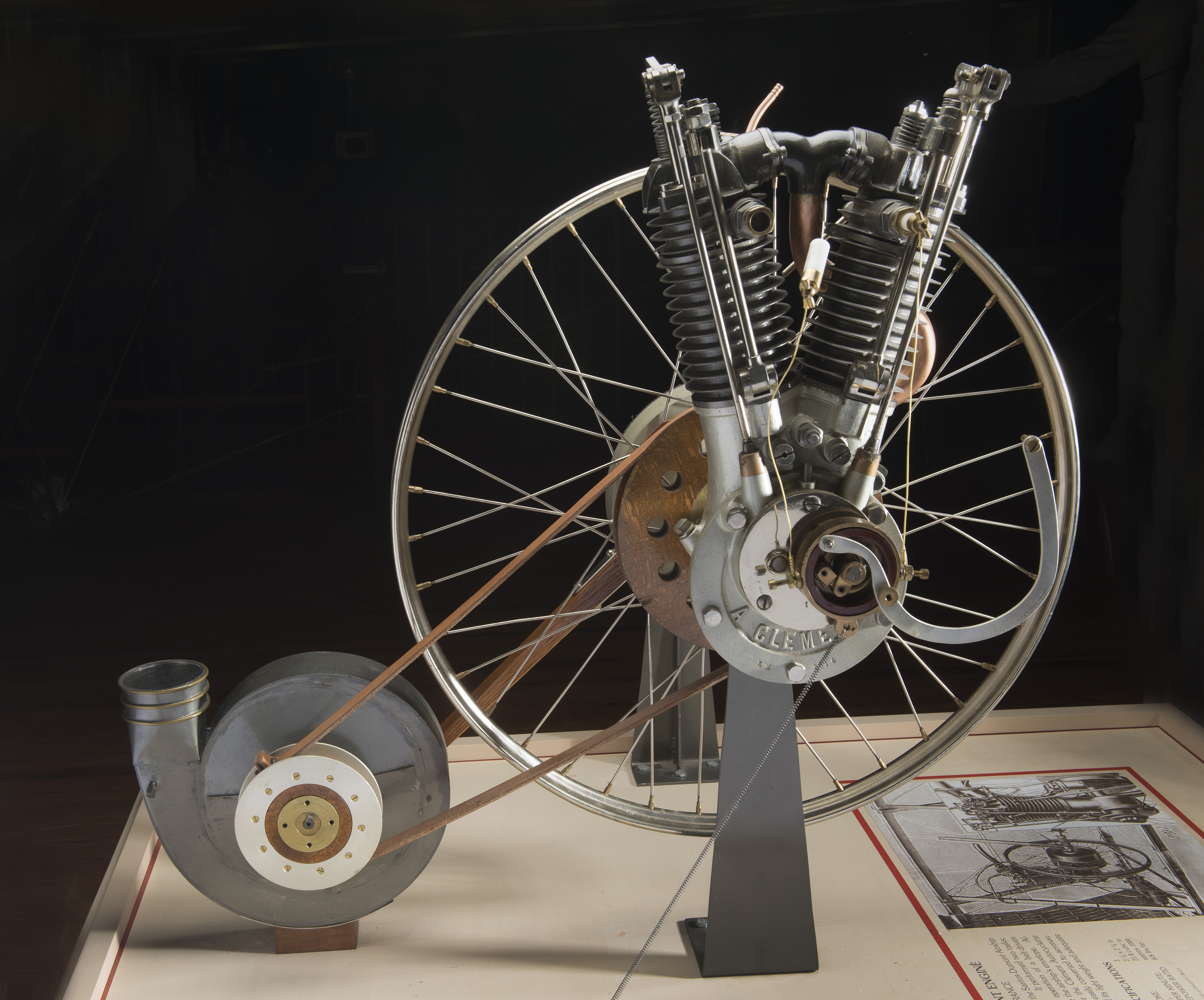 A compact two-cylinder engine with a crankshaft, external flywheel, pulley, leather belt, and blower equipment.