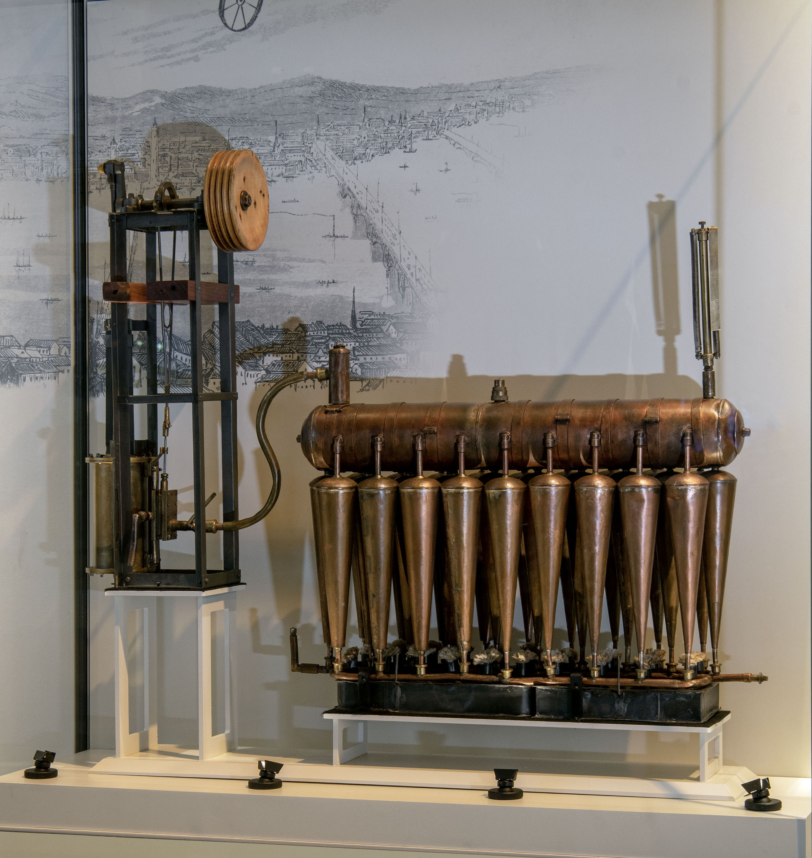 A compact single-cylinder steam engine with a boiler, expansion tubes, slide valve, piston, pulley, and open steel frame.