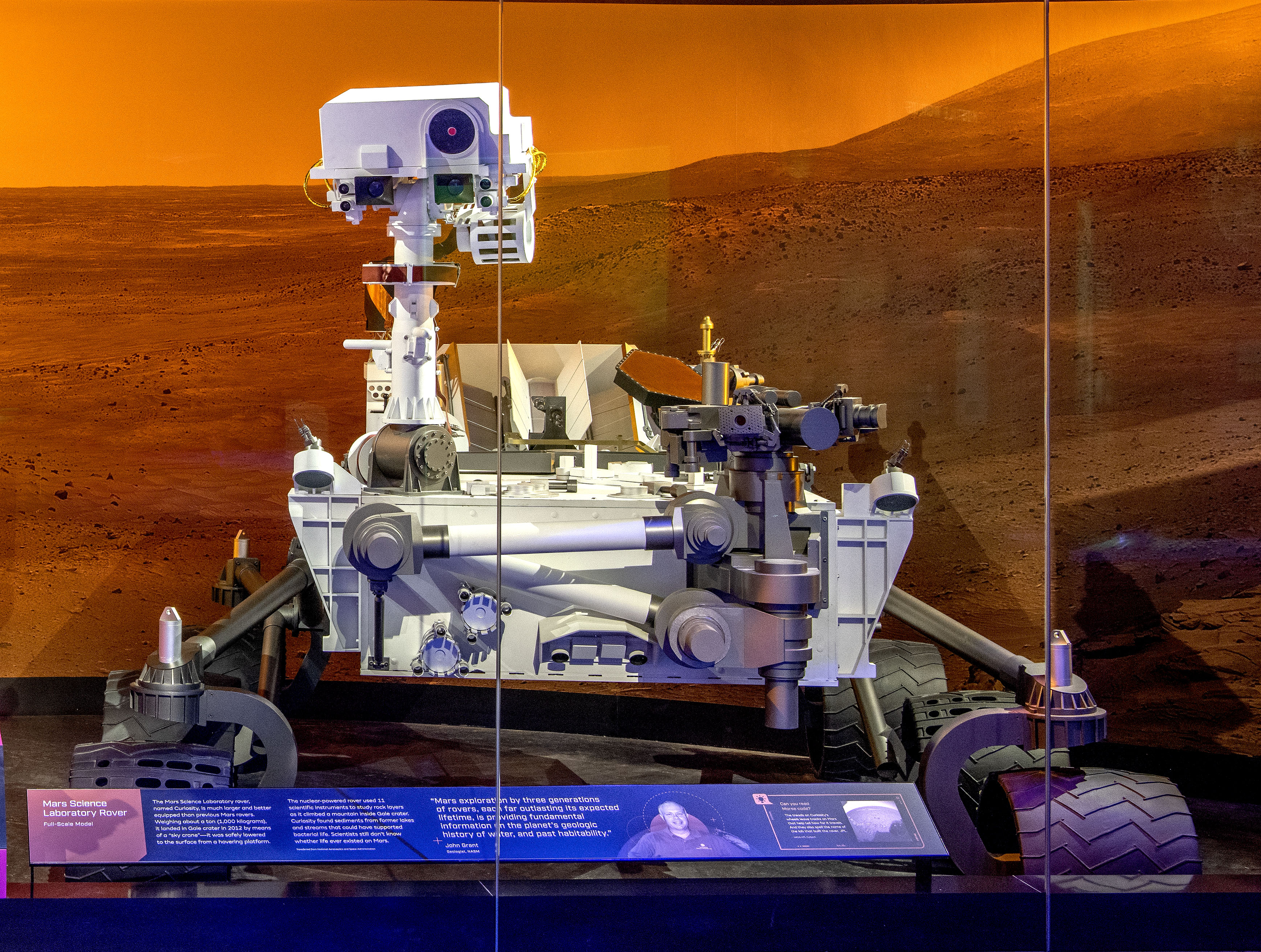 Full-scale six-wheeled Curiosity rover model with a white equipment deck, tall camera mast, and articulated robotic arm.