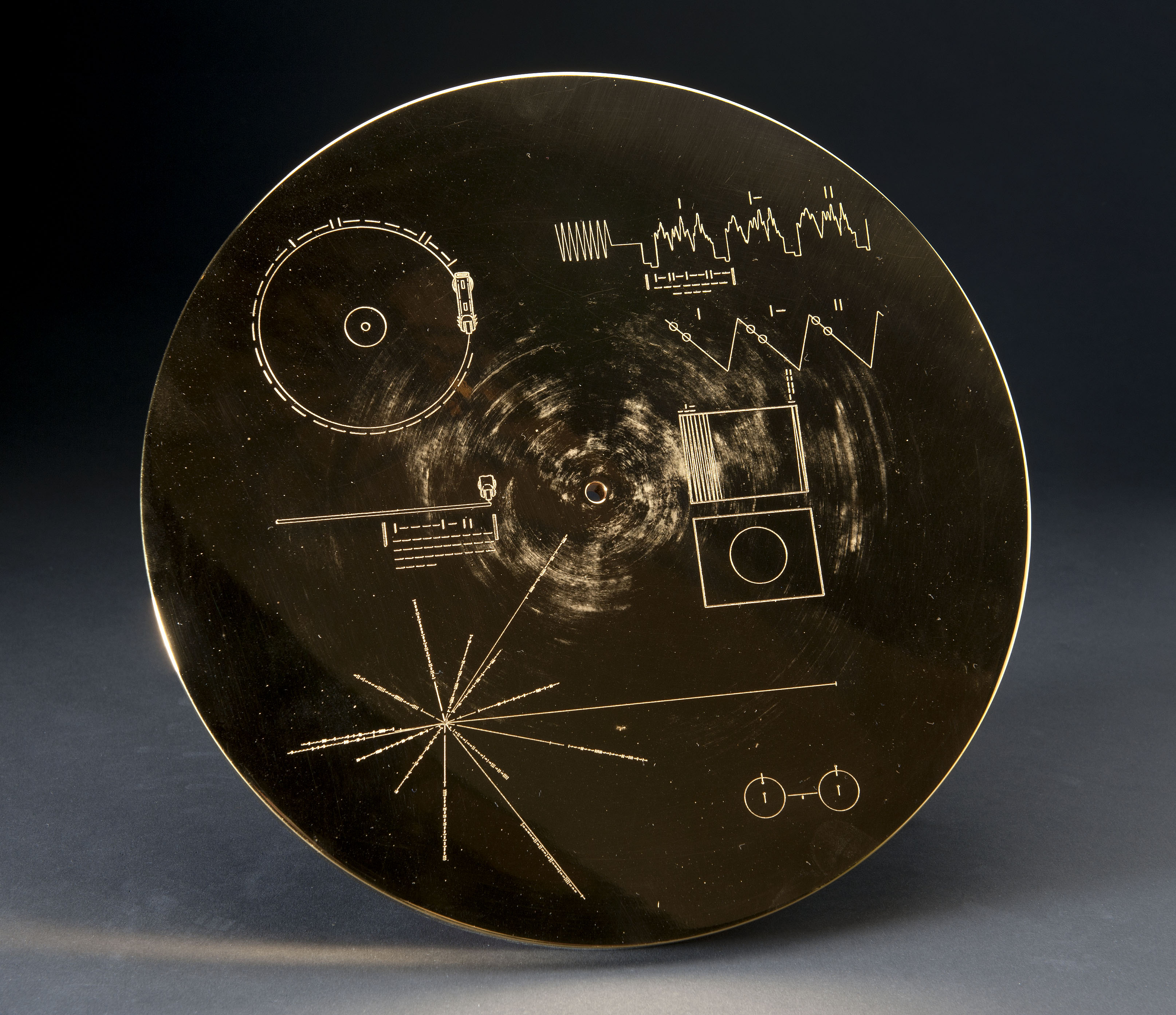 Circular gold-colored record cover engraved with diagrams intended to explain time, playback, images, and the Sun’s location.