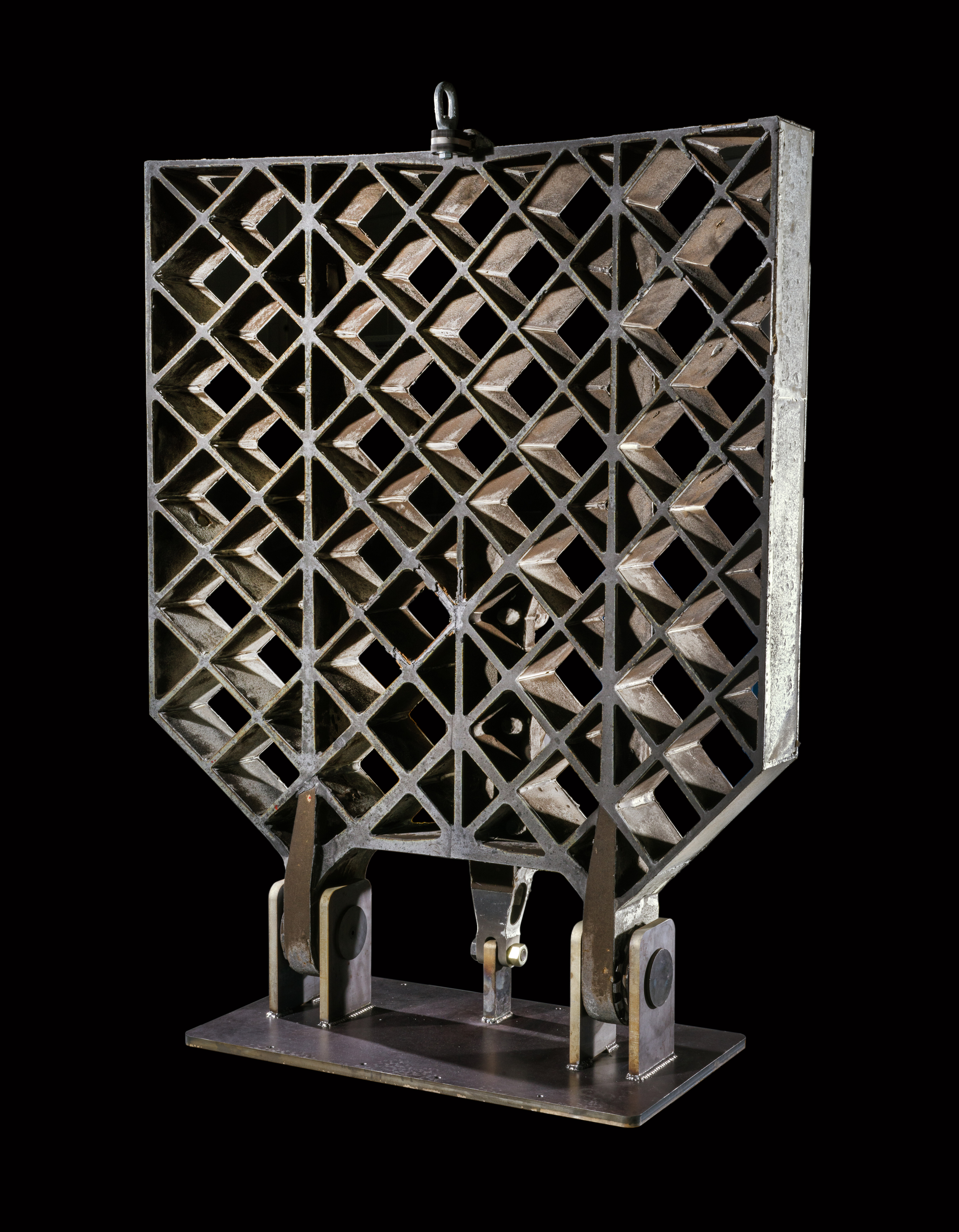A large hinged metal grid fin shaped like a paddle, with a lattice of square openings that lets air pass through.