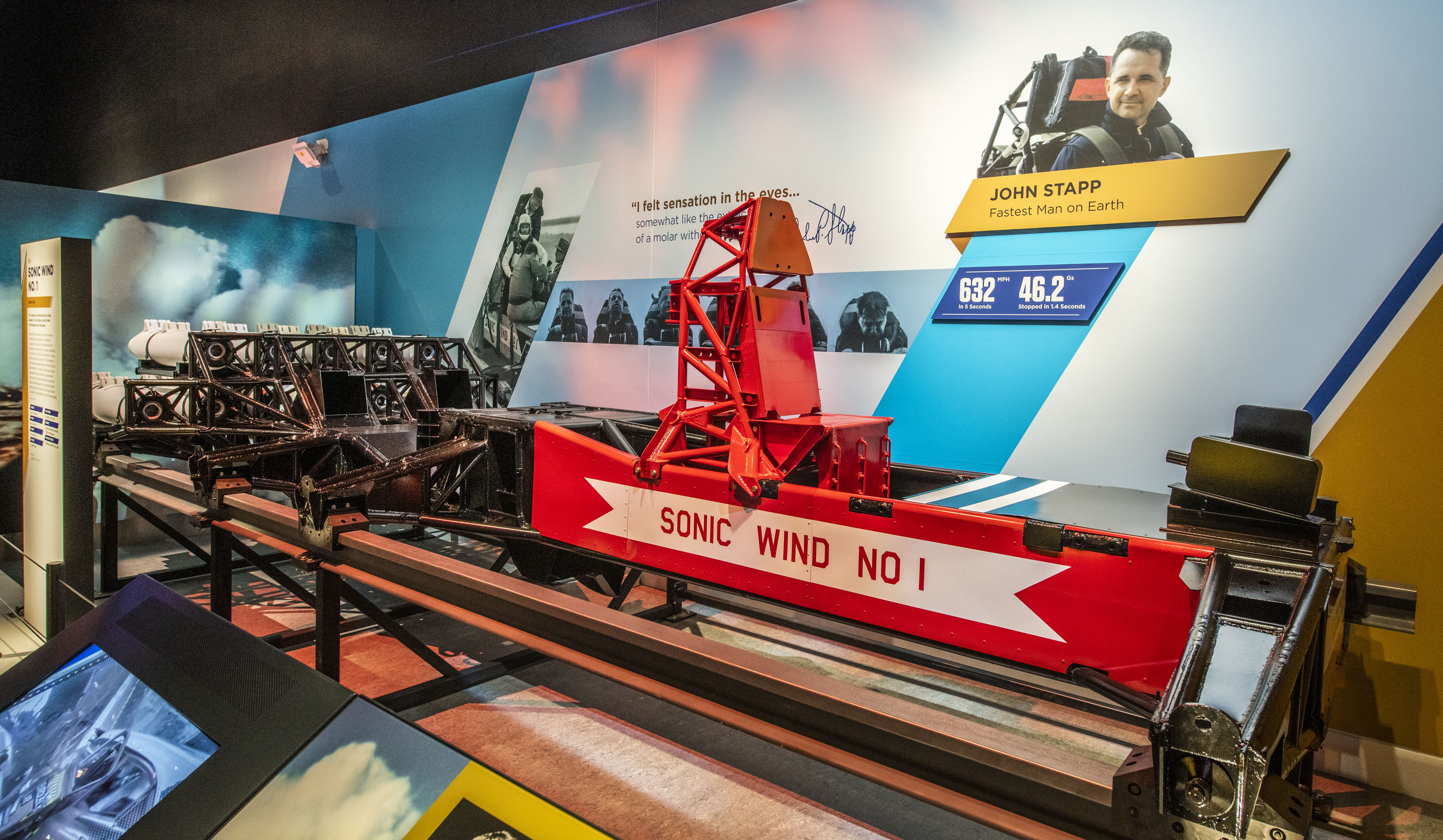 Red rocket sled with a high-backed seat, black frame, twin rails, and nine solid-fuel rockets mounted behind the rider.