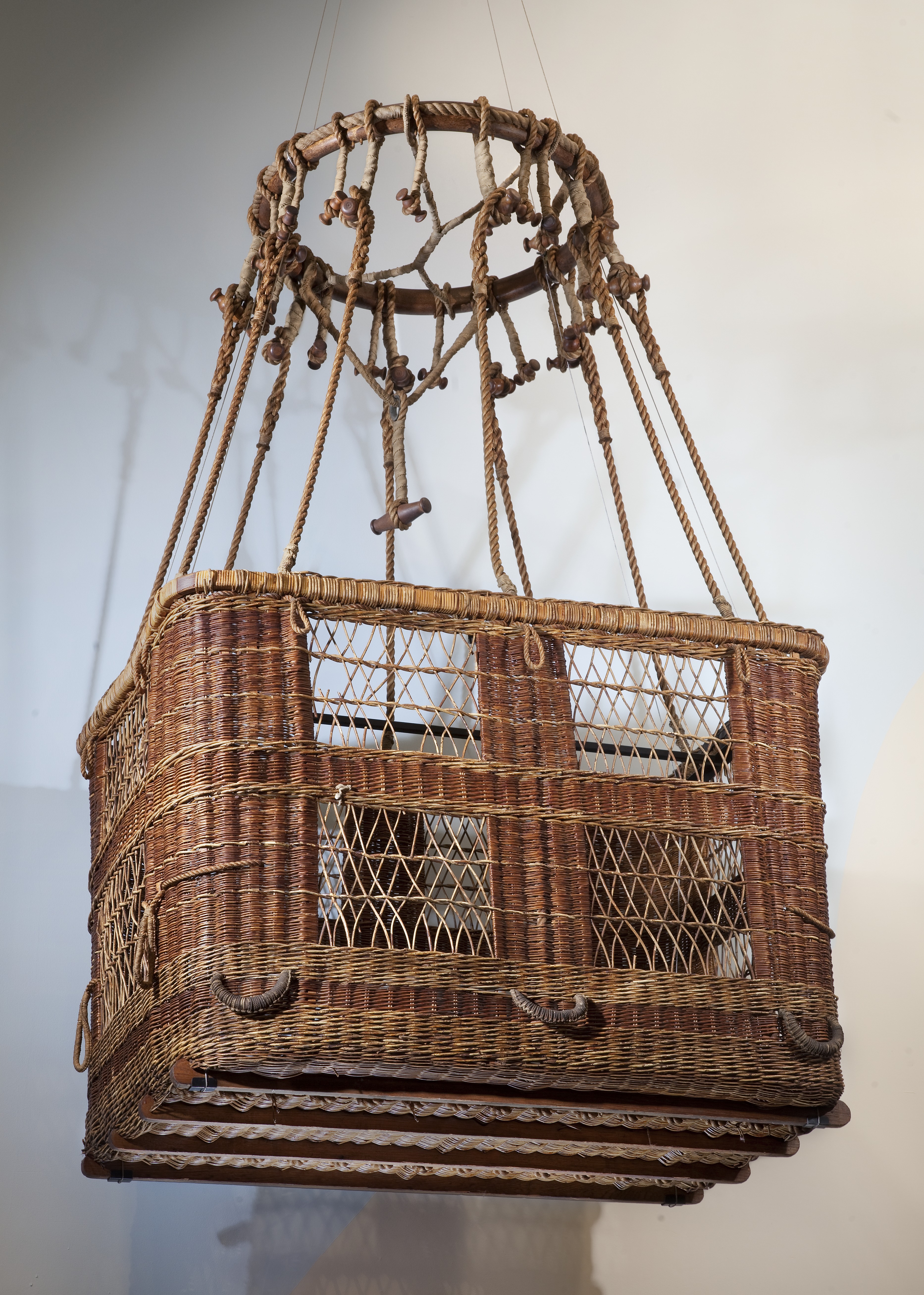 Brown wicker balloon basket fitted with wood, rope, and metal equipment.