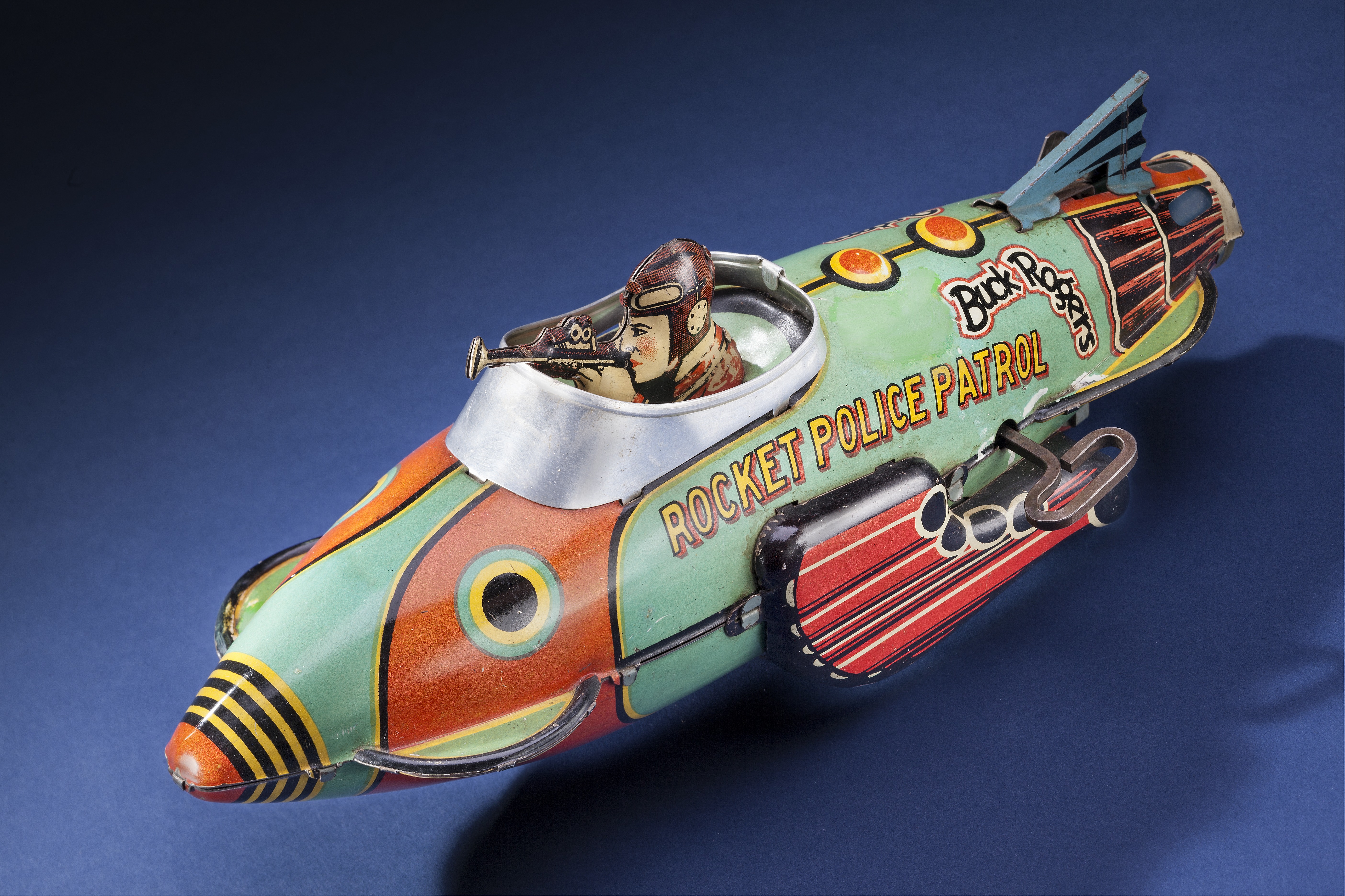 Colorful Buck Rogers wind-up rocket ship toy displayed with other 1930s space-themed toys.