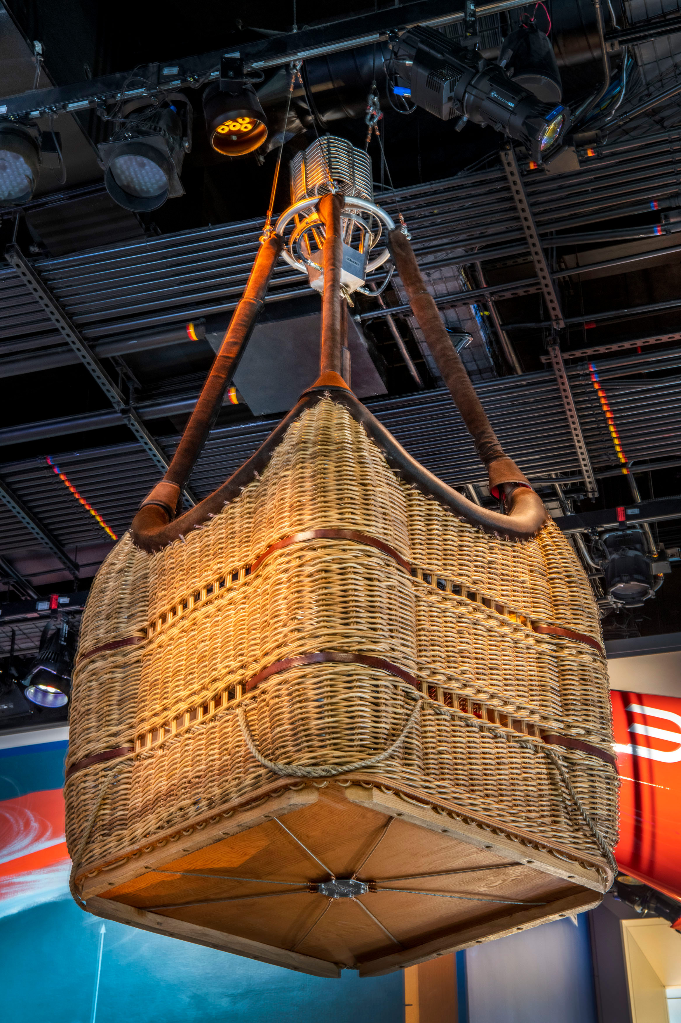 Square wicker balloon basket with leather trim, fuel tanks, steel suspension cables, and flight instruments.