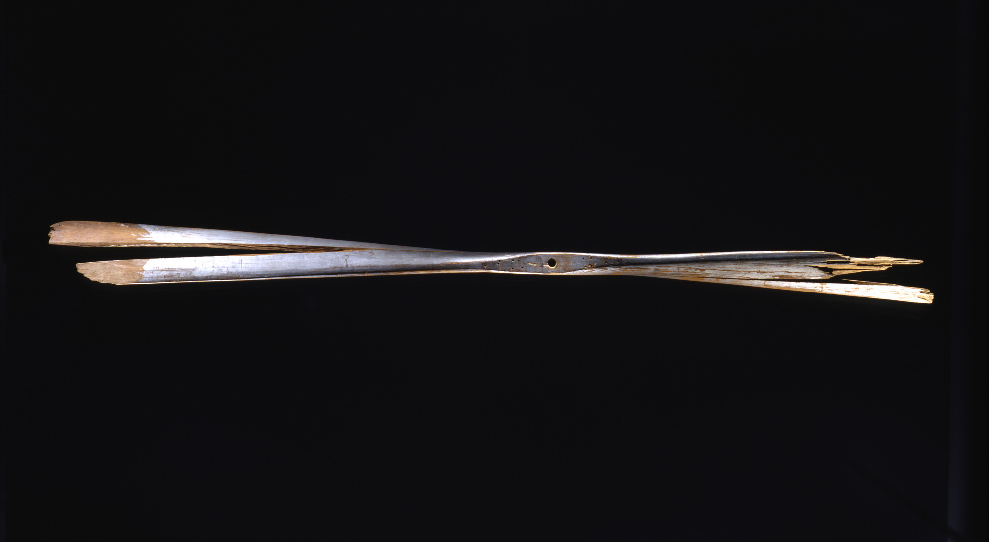 Damaged two-blade fixed-pitch wooden propeller split lengthwise, with silver coating and a central mounting hole.