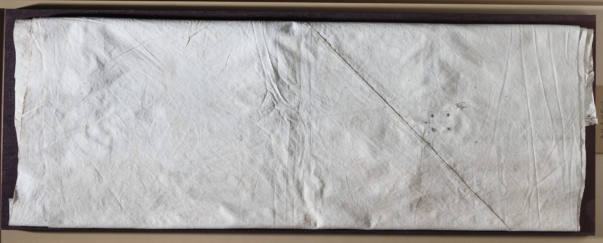 Panel of unbleached muslin with seams, stains, and small symmetrical attachment holes.